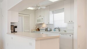 Une cuisine moderne avec des meubles blancs, un four à micro-ondes encastré, un grille-pain et un lave-vaisselle.