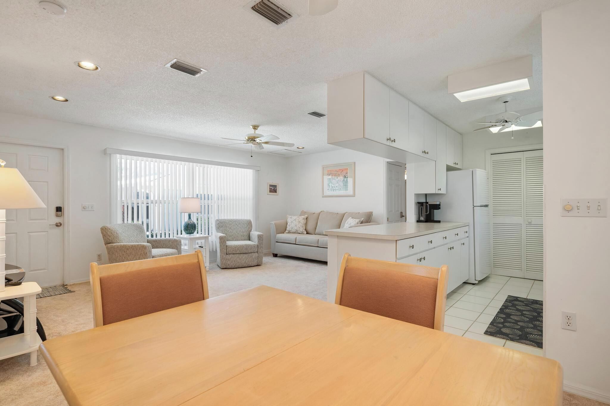 Una cocina moderna con armarios blancos, un comedor con mesa de madera y una sala de estar con sofá y sillones.