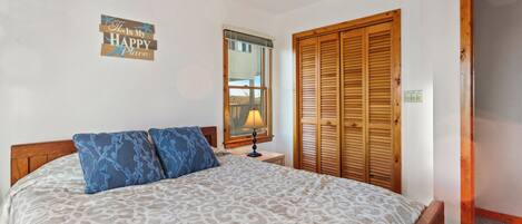 A bedroom with a bed, a nightstand, a lamp, a wooden wardrobe, and a wall sign.