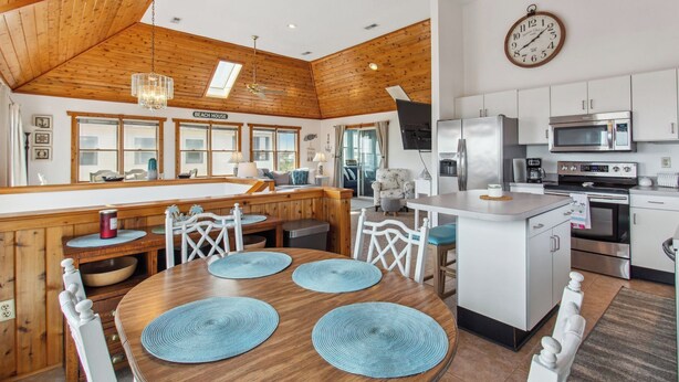 A spacious kitchen with modern appliances, a dining area with wooden furniture, and a large window overlooking the beach. - 5064 McBride's Shore Thing * 2 Min Walk to Beach (Kill Devil Hills)