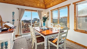 A dining area with a wooden table and chairs, a vase with plants, and a view of the sea through large windows. - 5064 McBride's Shore Thing * 2 Min Walk to Beach (Kill Devil Hills)