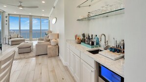 A modern kitchen with a built-in dishwasher, a glass shelf with kitchenware, and a view to the outside. - Penthouse Paradise at The Pearl! (Navarre Beach)