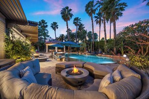 A pool area with a fire pit, lounge chairs, and a covered seating area surrounded by palm trees. - Cabana Palms - A half acre desert oasis (Indio)