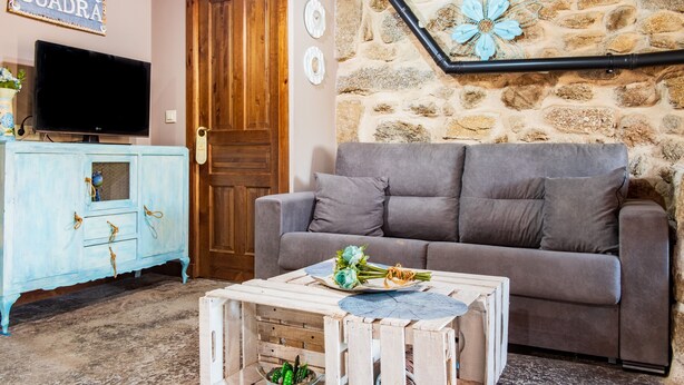 Una sala de estar con pared de piedra, un sofá gris, un aparador de madera y un televisor.