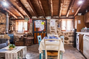 A rustic stone interior with a wooden ceiling, a dining table set with blue plates, a washing machine, and a rustic fireplace. - Holiday Home 'La Cuadra' with Mountain Views (Villar De Corneja)