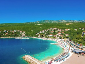 A coastal town with a beach, clear turquoise waters, and houses on a hillside.