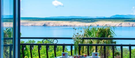 Un balcón con una mesa lista para dos, con vistas a un lago y montañas a la distancia.