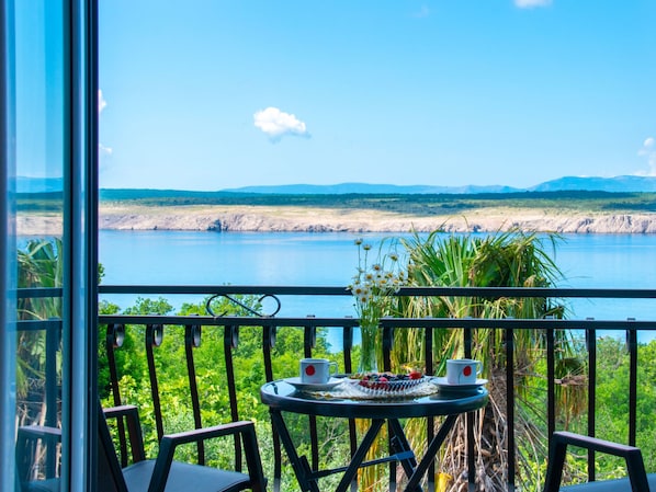 A balcony with a table set for two, overlooking a lake with distant mountains.