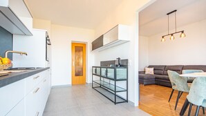 A modern kitchen with grey tiles, a wooden door, and a dining area with a grey sofa and striped chairs. - Snjezana by Interhome (Crikvenica/Jadranovo)