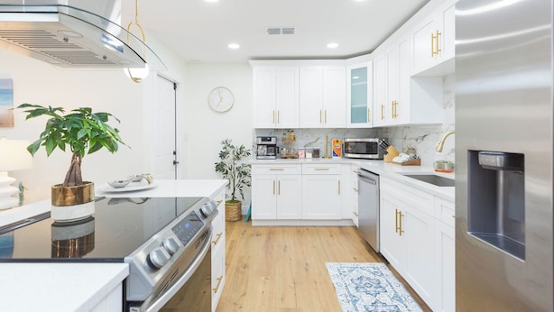 A modern kitchen with white cabinets, stainless steel appliances, and a wooden floor. - MADEIRA BEACH RETREAT WITH HEATED POOL. (Seminole)