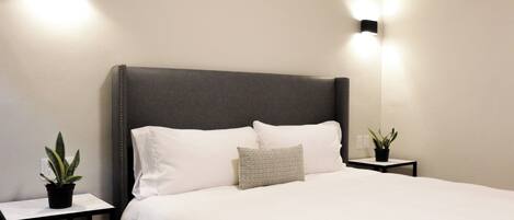 A neatly made bed with a grey headboard, two bedside tables with potted plants, and wall-mounted lights.