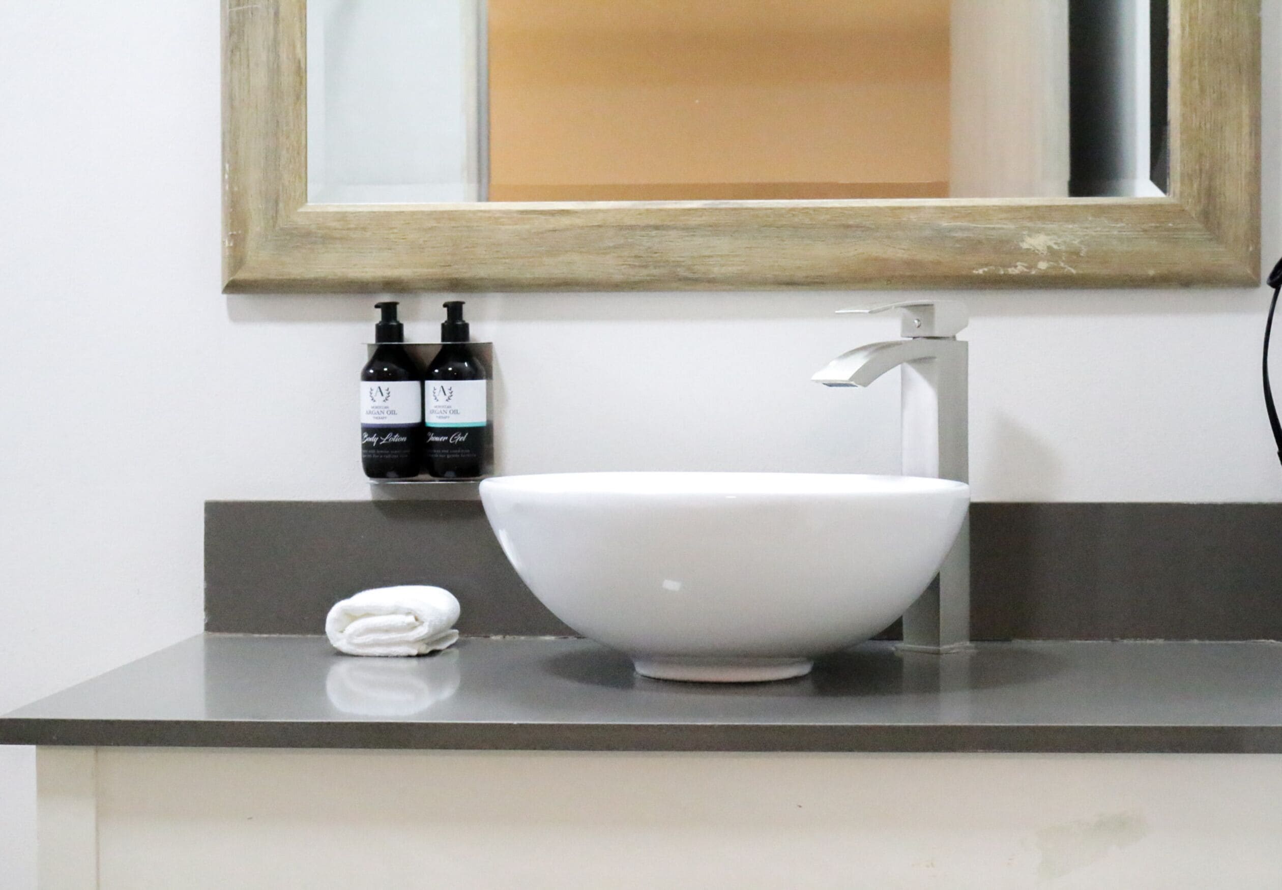 A bathroom with a white sink, a mirror, and two bottles of shampoo on the wall.