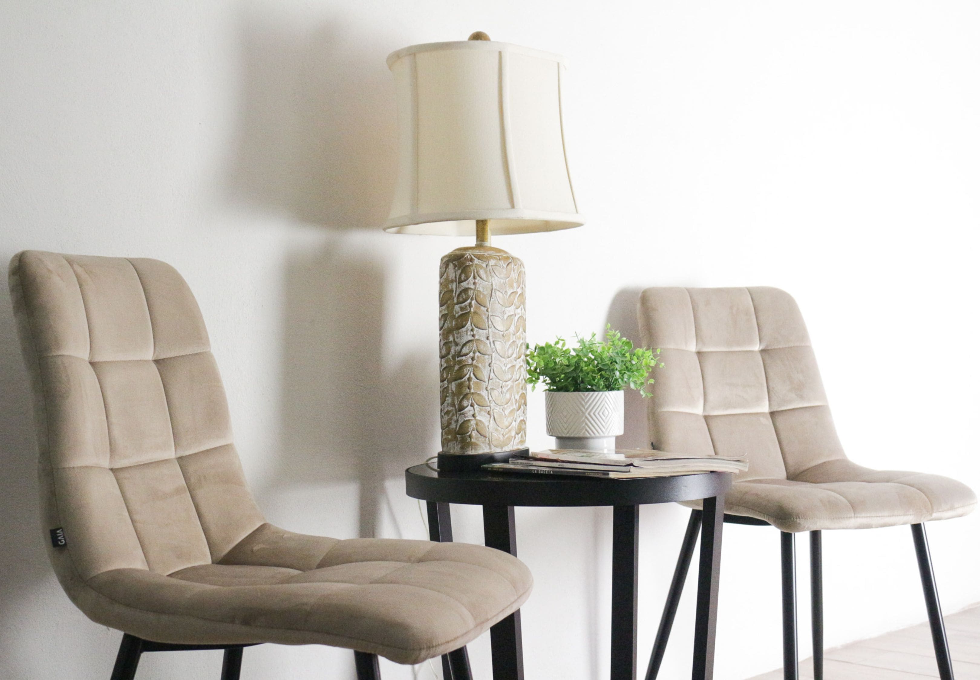 Dos sillones tapizados en beige, una mesa con una lámpara y una planta en maceta.