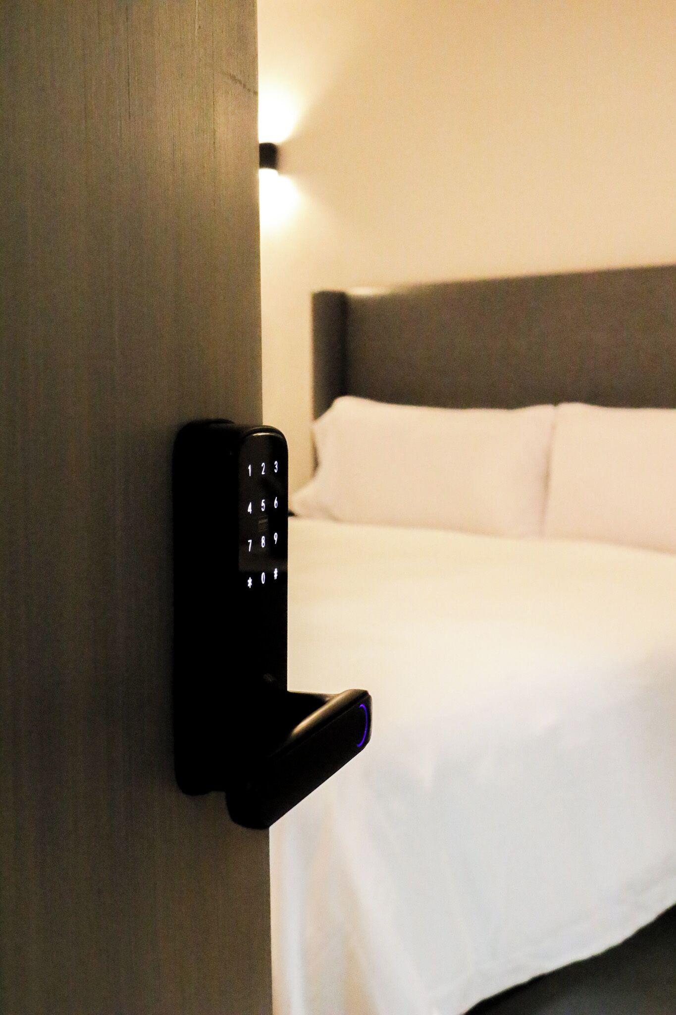A modern hotel room with a wall-mounted control panel and a neatly made bed.