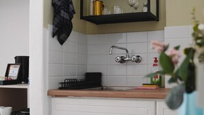 A kitchen with white cabinets, a black shelf with dishes, a faucet, and a vase with flowers. - Room 'Studio 3' with Private Terrace, Wi-Fi and Air Conditioning (Paros)