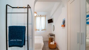 A hotel room with a glass shower enclosure, a bed, a television, and a small table with a basket. - Studio Apartment '5' with Private Terrace, Wi-Fi and Air Conditioning (Paros)