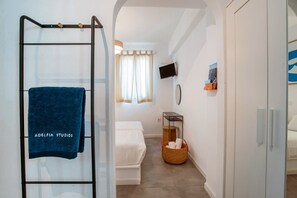 Une chambre d’hôtel avec une douche en verre, un lit, une télévision et une petite table avec un panier.