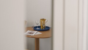 A narrow hallway with a framed artwork on the wall, a small table with a glass, a cup, and a magazine, and a white chair. - Studio Apartment '5' with Private Terrace, Wi-Fi and Air Conditioning (Paros)