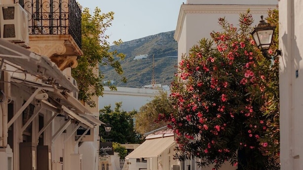 Une rue étroite aux pavés, bordée de bâtiments blancs, d’où l’on aperçoit une étendue d’eau au loin.