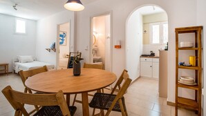 A dining area with a round wooden table, chairs, a hanging light fixture, and a kitchen visible through an archway. - Studio Apartment '2' with Private Terrace, Wi-Fi and one Air Condition in the bedroom (Paros)