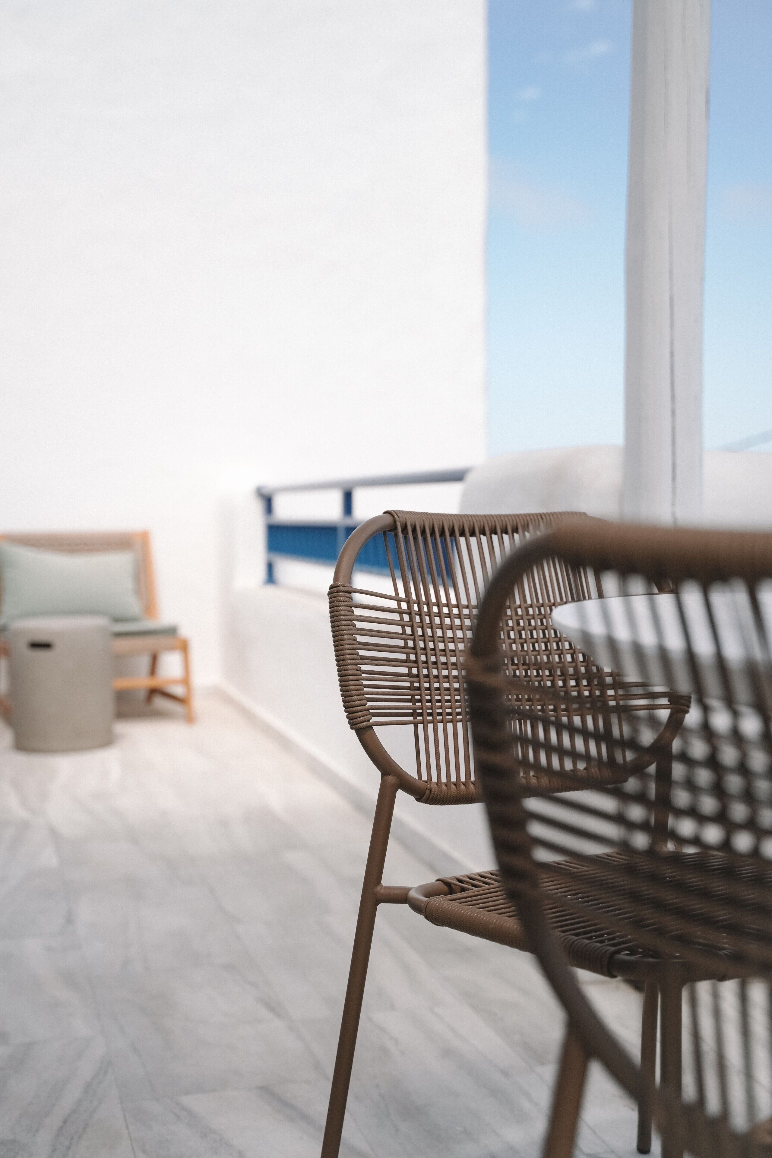 Ein Korbstuhl mit Blick auf einen Balkon und ein Bett mit Kissen.
