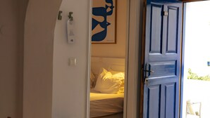 Ein Zimmer mit einem Bett, einer blauen Tür, einer weißen Wand mit einem gerahmten Bild und einem kleinen Tisch mit einem blauen Teller.