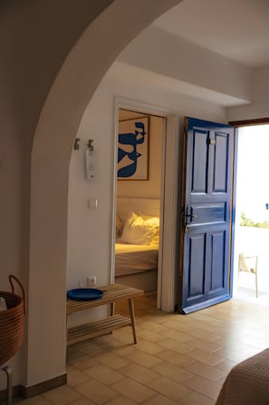 A room with a bed, a blue door, a white wall with a framed picture, and a small table with a blue plate.