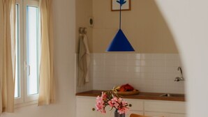 Ein Essbereich mit Holztisch und Stühlen, einer Blumenvase, einer blauen Pendelleuchte und einem Fenster mit Vorhängen.