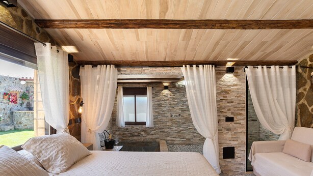 Quarto com cama, sofá, parede de pedra e janela.