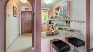 A modern kitchen with a bar area, wooden cabinets, and a countertop with a wine bottle and glasses. - Vacation Apartment 'The Sunset' with Shared Pool, Wi-Fi and Air Conditioning (Costa Adeje)
