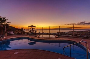 A swimming pool with a view of the sunset and cityscape.