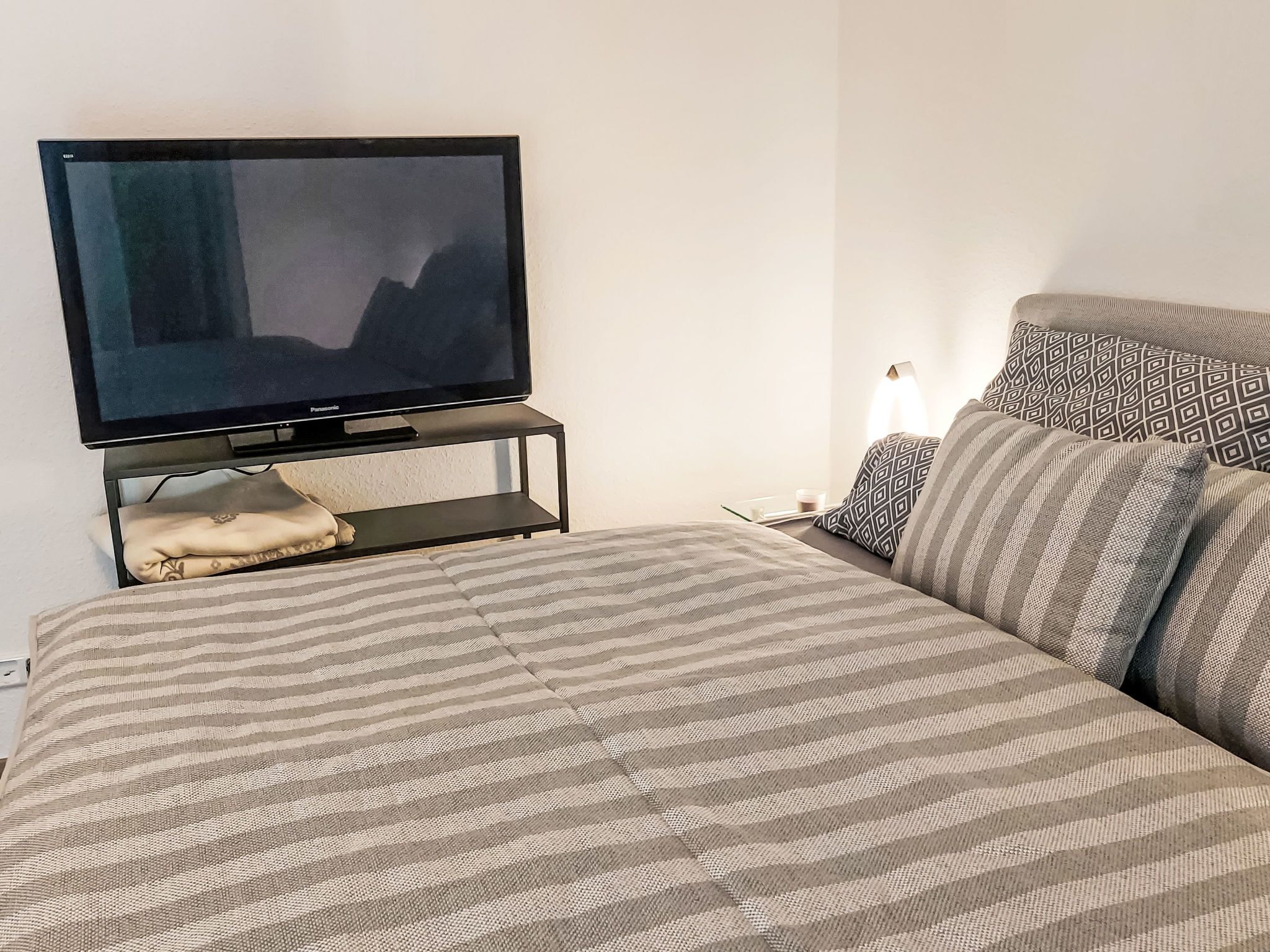 Une chambre à coucher bien rangée, avec un lit, un téléviseur posé sur un meuble et une table de chevet avec une lampe.