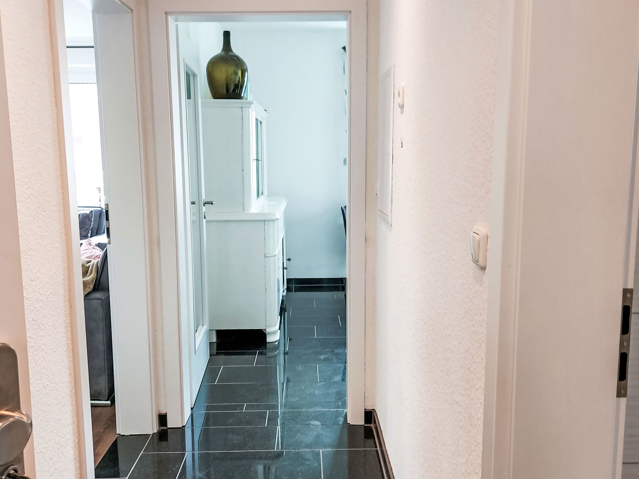 Ein Flur mit einem weißen Schrank, einer Vase darauf und einem schwarzen Kachelboden.