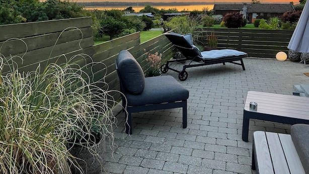 A patio with a lounge chair, a small table, and a view of the sunset over a body of water. - Cozy summerhouse with spectacular views! (Ølsted)