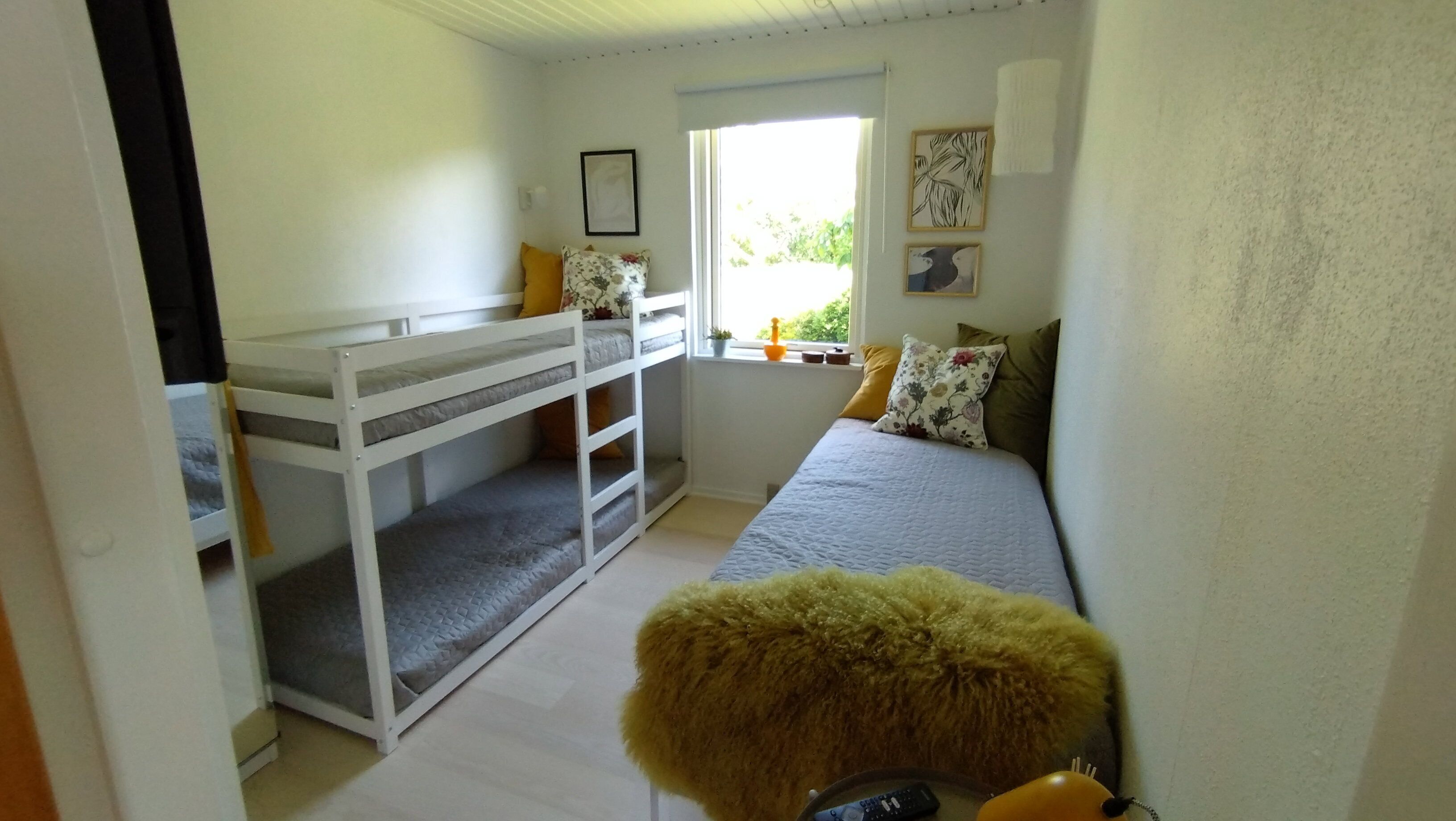 Ein Schlafzimmer mit Etagenbetten, einem Bett mit Kissen, einem Fenster mit Aussicht und einem kleinen Tisch mit einer Pflanze.