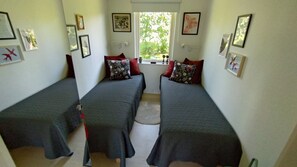Ein Zimmer mit zwei Einzelbetten, einem Fenster mit Blick auf Grünflächen und verschiedenen gerahmten Bildern an den Wänden.