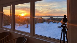 A room with a telescope on a tripod, large windows with a view of a snowy landscape and sunset. - Cozy summerhouse with spectacular views! (Ølsted)
