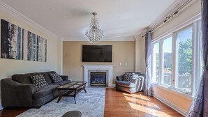A living room with a fireplace, a sofa, a coffee table, and a large window. - Harmony House: 7-BR Multi family & Group Oasis with Dual Living (Richmond Hill)
