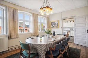 A dining room with a round table, chairs, a chandelier, and a view of the outside.