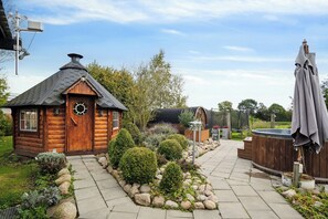 A wooden cabin with a chimney, a hot tub, and a stone pathway.