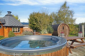 A hot tub in a wooden outdoor setting with a wooden cabin and a barrel in the background.