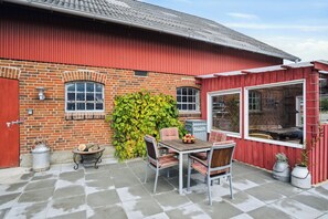 A patio with a table and chairs, a red barn, and a brick wall. - Country idyll with wilderness bath and sauna (Haderslev)