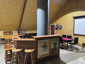 A bar area with stools, a dartboard, and a projector screen.