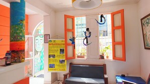 A room with a wooden bench, a window with orange shutters, and a mural on the wall. - SOLCITY HOSTEL (Salvador)