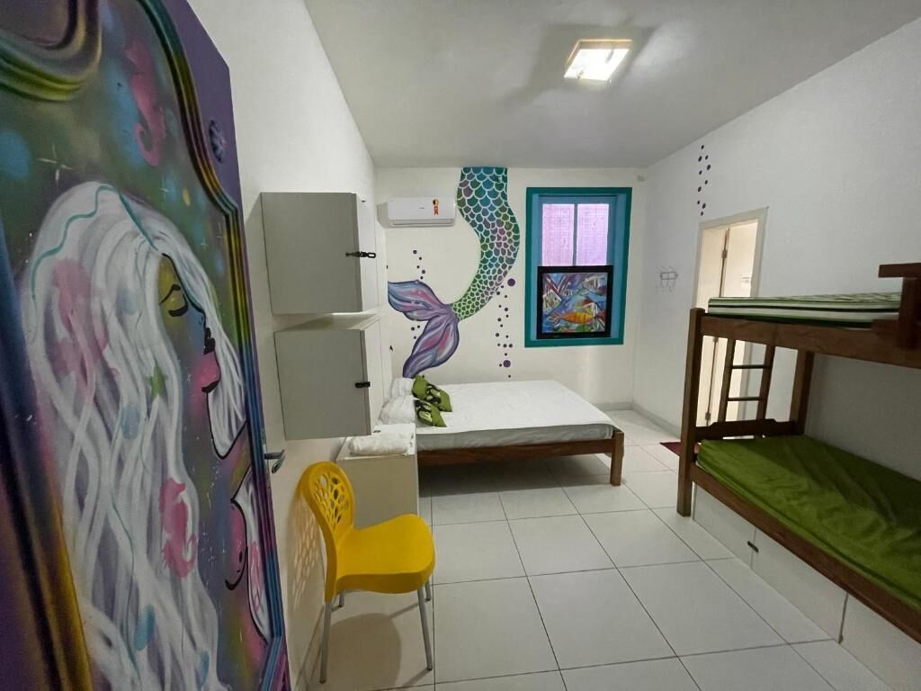 A bedroom with a bed, a chair, a bunk bed, a window, and a wall mural.
