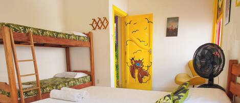 A room with a bunk bed, a single bed, a ladder, a fan, and a door with a colorful design.
