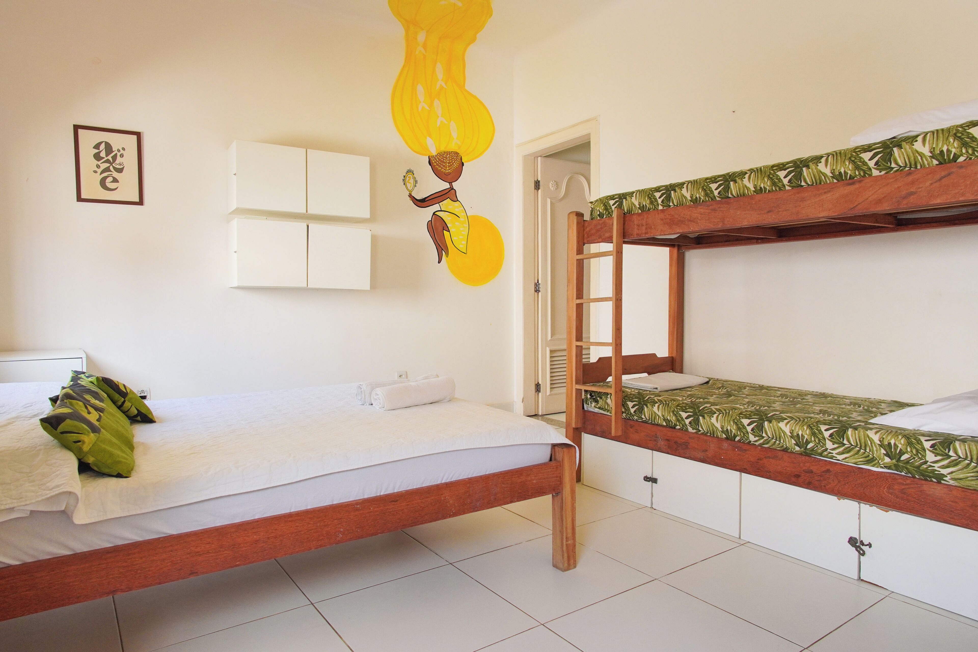 A room with a bunk bed, a single bed, a wall-mounted cabinet, and a door leading to another room.