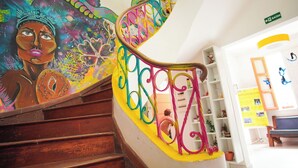 A staircase with a colorful railing and a mural on the wall. - SOLCITY HOSTEL (Salvador)