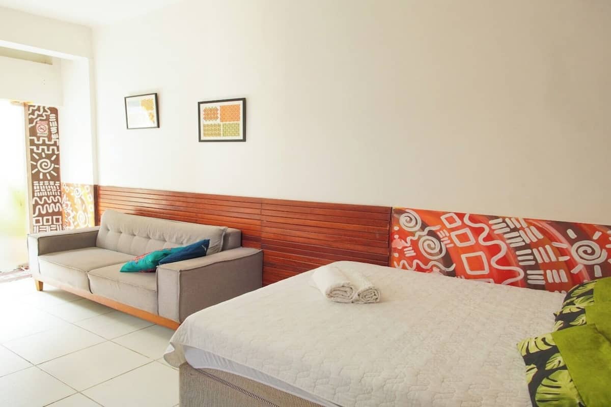 A hotel room with a sofa, a bed, and a wooden headboard. There are two framed pictures on the wall.