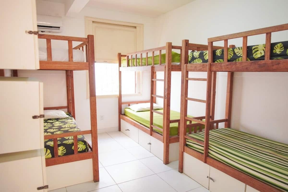 A dormitory room with bunk beds, a small kitchenette, and a window.